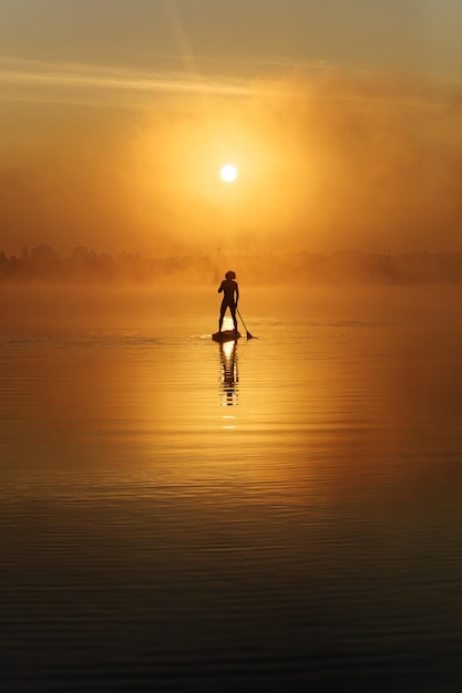 Young man practising in sup surfing during amazing sunrise