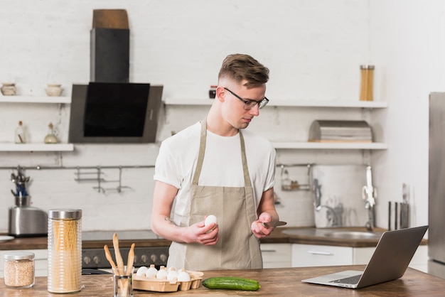 Young man preparing the food by looking at his laptop on table