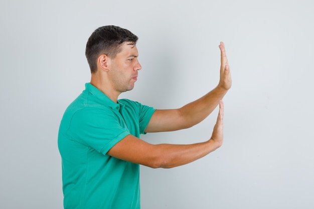 Free photo young man pushing something with hands in green t-shirt and looking serious. .