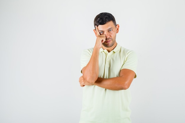 Young man putting finger prop up on forehead in t-shirt and looking careful.