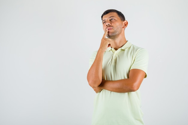 Young man putting finger prop up on mouth in t-shirt and looking thoughtful