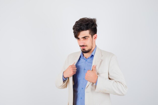 Young man putting hands on jacket in blue shirt and white suit jacket and looking happy