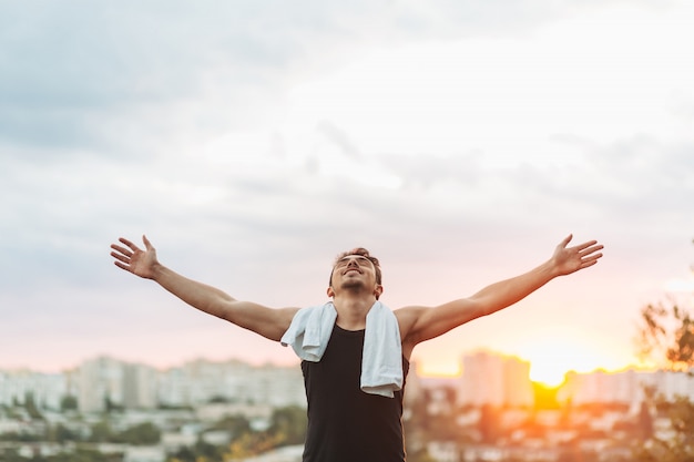 Young man raising hands over sunset sky after training