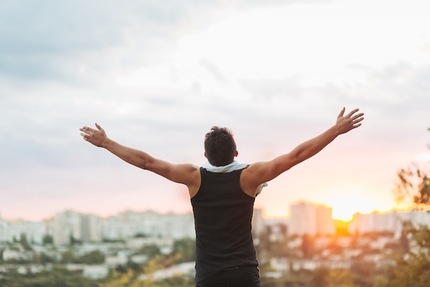 Young man raising hands over sunset sky after training