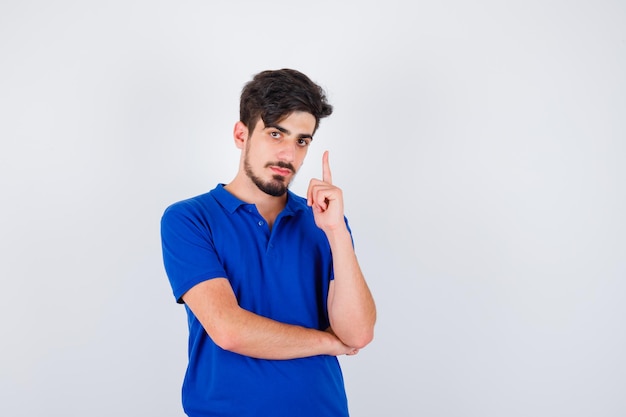 Young man raising index finger in eureka gesture in blue t-shirt and looking serious