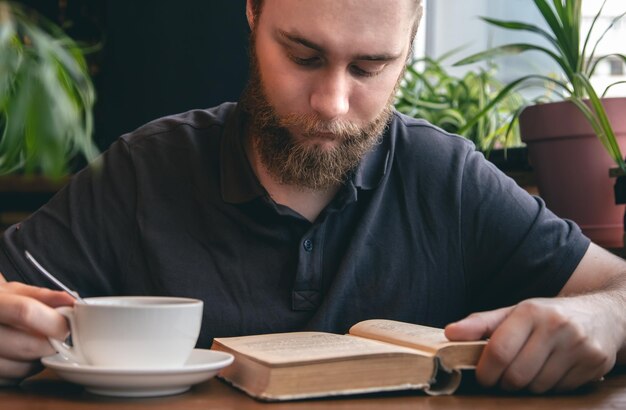 A young man reads a book over a cup of tea in a cafe