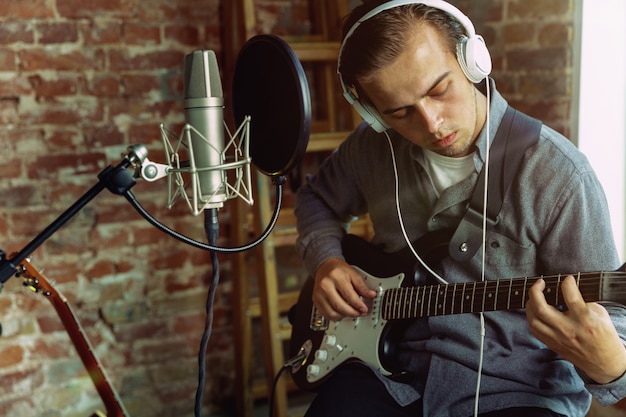 Free photo young man recording music, playing guitar and singing at home