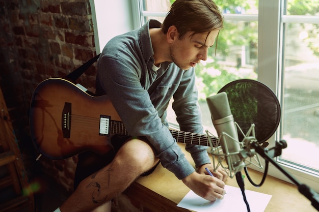 Young man recording music video blog, home lesson or song, playing guitar or making broadcast internet tutorial while sitting in loft workplace or at home