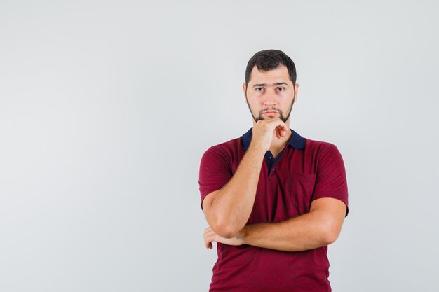 Young man in red t-shirt looking forward and looking concentrated , front view.