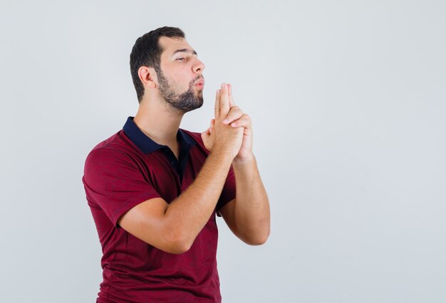 Young man in red t-shirt showing pistol sign and looking assured , front view.