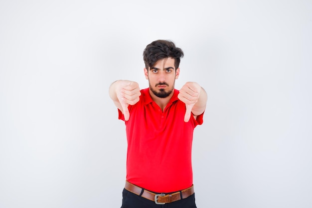 Young man in red t-shirt showing thumbs down with both hands and looking serious