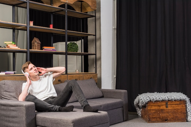 Free photo young man relaxing on sofa listening music on headphone at home