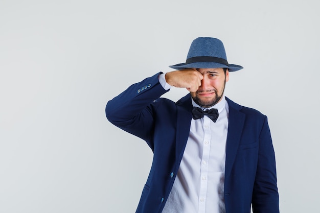 Free Photo young man rubbing eye while crying in suit, hat front view.