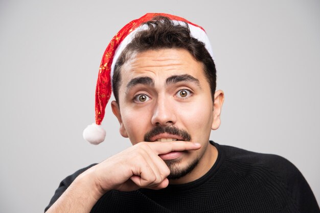 Young man in Santa's hat biting his finger .