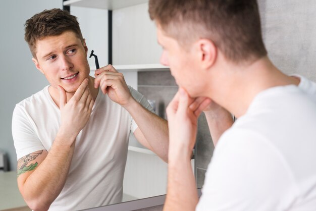 Young man shaving in front of mirror in bathroom