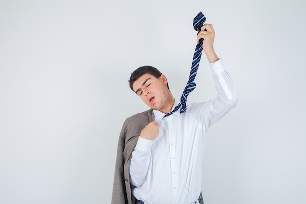 Young man in shirt, jacket, striped tie making suicide gesture with tie and looking hopeless