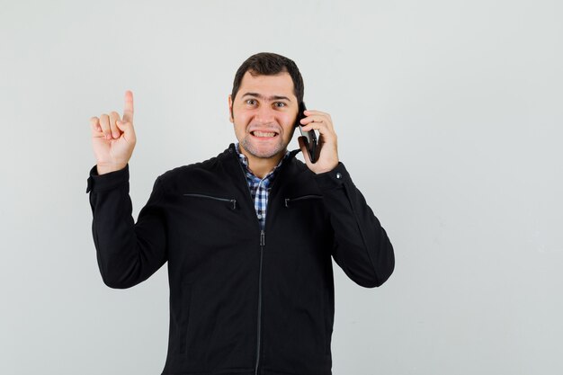 Young man in shirt, jacket talking on mobile phone, pointing up and looking cheerful