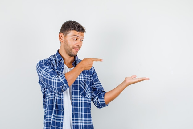 Young man in shirt pointing finger to spread palm , front view.