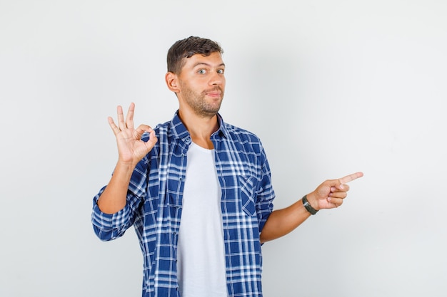 Young man in shirt showing ok sign while pointing away , front view.