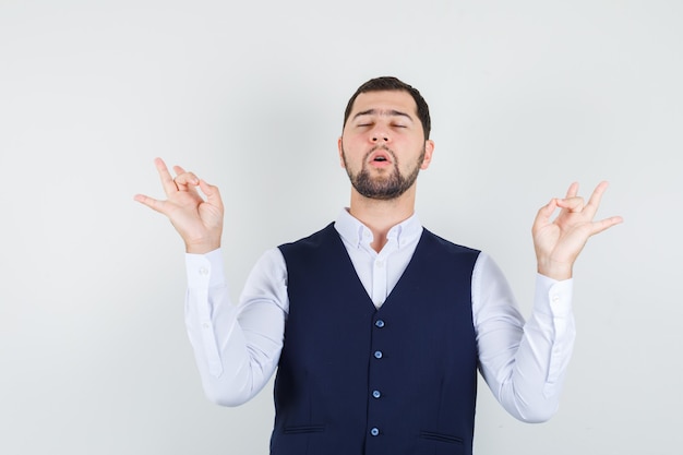 Young man in shirt, vest doing meditation with closed eyes and looking relaxed