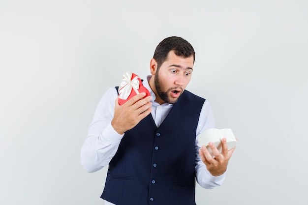 Free photo young man in shirt, vest looking into present box and looking amazed