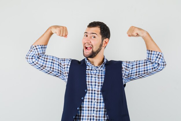 Young man in shirt, vest showing his muscles and looking powerful , front view.