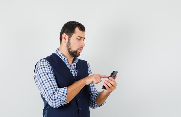 Young man in shirt, vest using mobile phone and looking busy , front view.