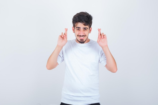 Young man showing crossed fingers in t-shirt and looking cute