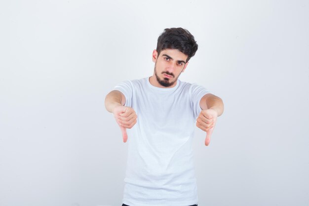 Young man showing double thumbs down in white t-shirt and looking confident