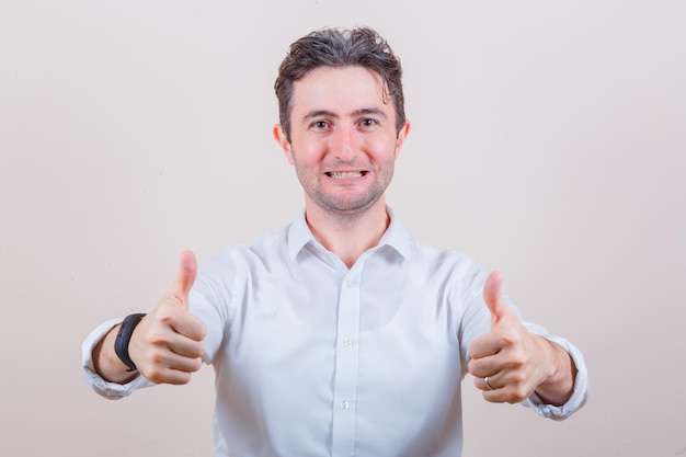 Free photo young man showing double thumbs up in white shirt and looking happy