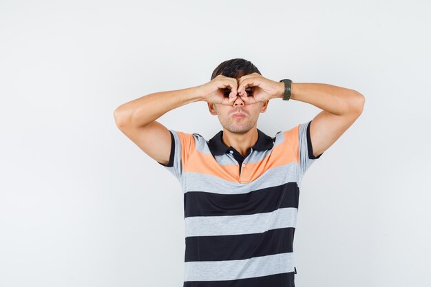 Young man showing glasses gesture in t-shirt and looking watchful