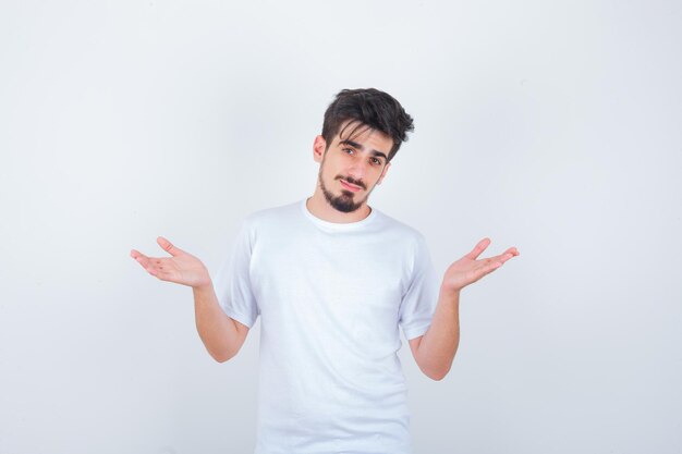 Young man showing helpless gesture in white t-shirt and looking confused