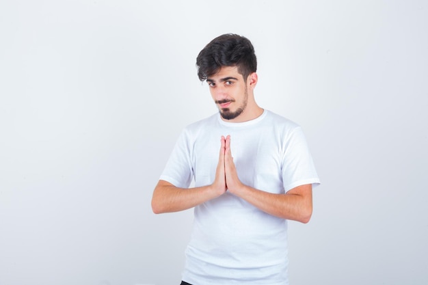 Young man showing namaste gesture in t-shirt and looking hopeful