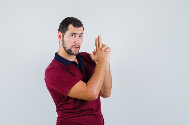 Young man showing pistol sign in red t-shirt and looking ready , front view.