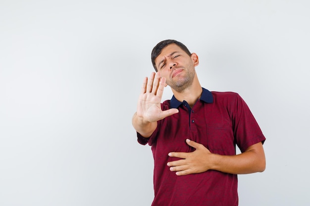 Young man showing refusal gesture in t-shirt and looking annoyed , front view.