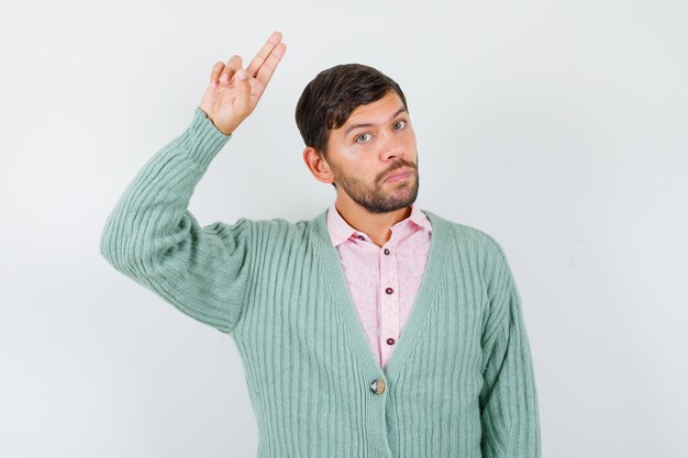 Young man showing salute gesture in shirt, cardigan and looking confident , front view.