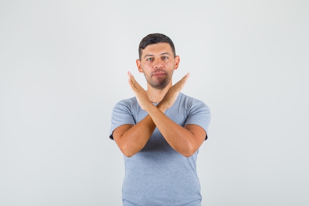 Free photo young man showing stop gesture with crossing hands in grey t-shirt and looking confident.