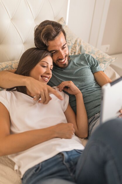 Young man showing tablet to girlfriend on bed