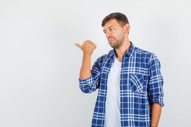 Young man showing thumb away in shirt and looking confused. front view.