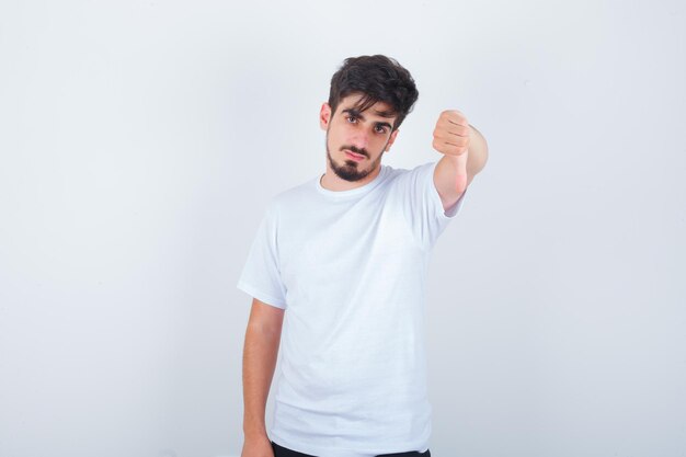 Young man showing thumb down in white t-shirt and looking confident