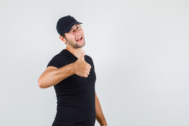 Young man showing thumb up and blinking eye in black t-shirt