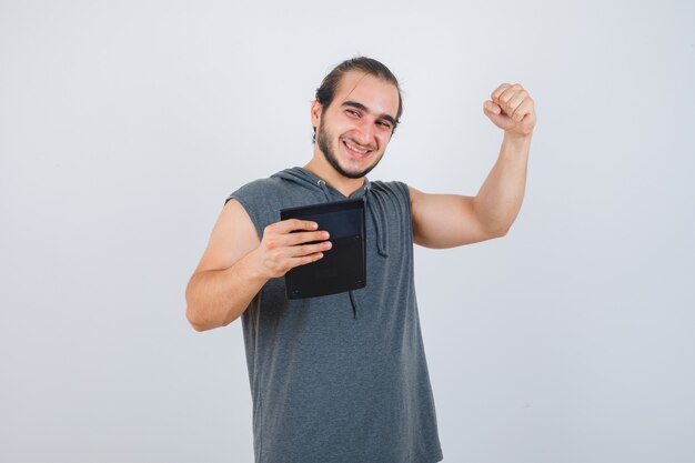 Young man showing winner gesture in hoodie and looking happy , front view.