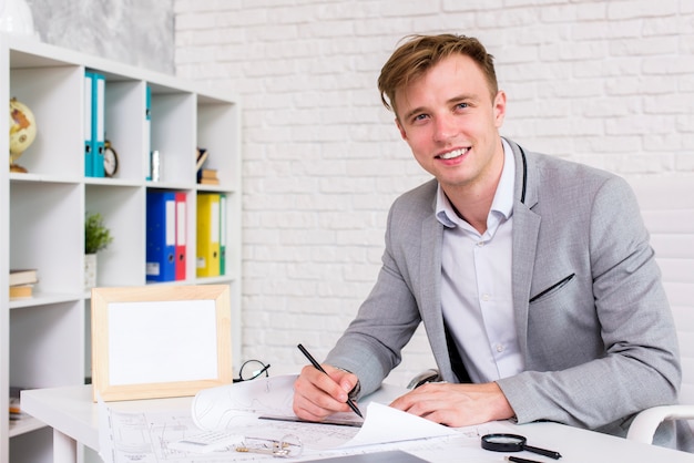 Young man signing a document while looking at the camera