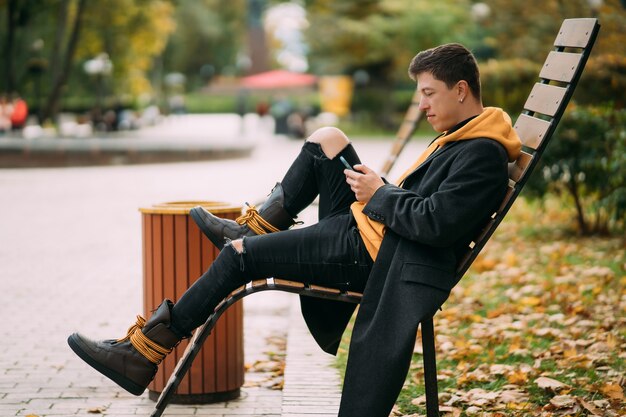 Young man sitting on a bench in park and listening to music