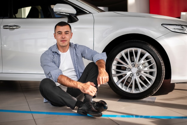 Young man sitting next to a car at dealership