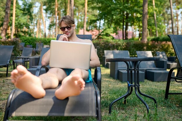 A young man sitting on a chaise longue with a laptop