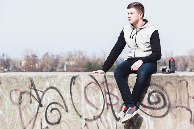 Young man sitting on graffiti wall