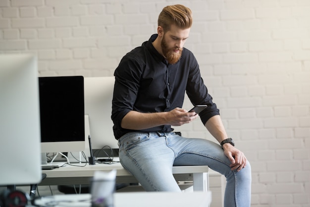 Free photo young man sitting on his desk and using mobile phone