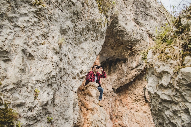 Free photo young man sitting on a rock and using his binoculars