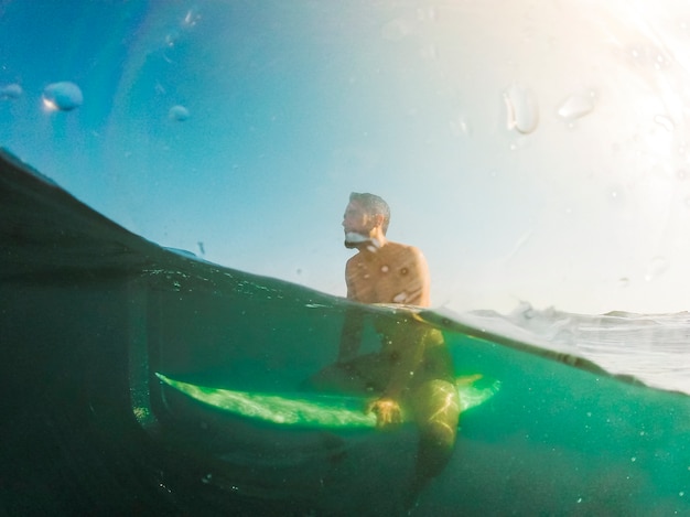 Free Photo young man sitting on surfboard in blue sea